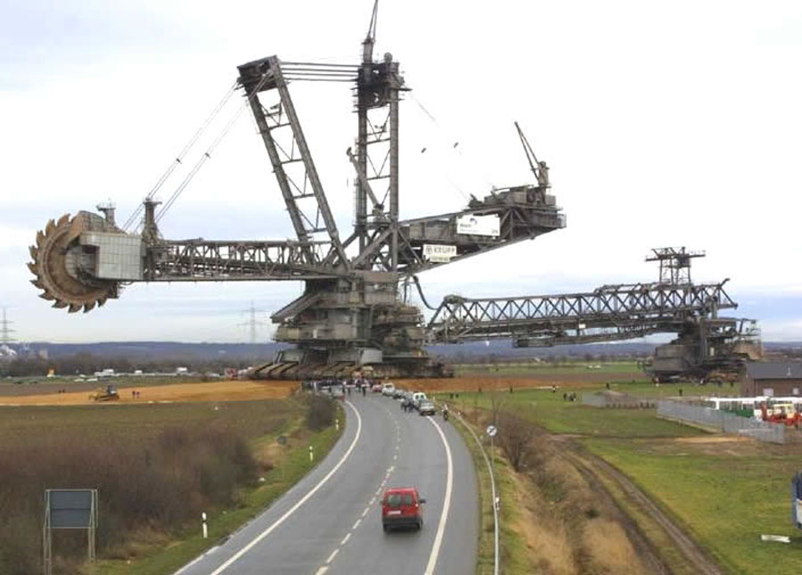 Ein riesiger Schaufelradbagger überquert eine Straße mit einer Geschwindigkeit von weniger als einem Kilometer pro Stunde.