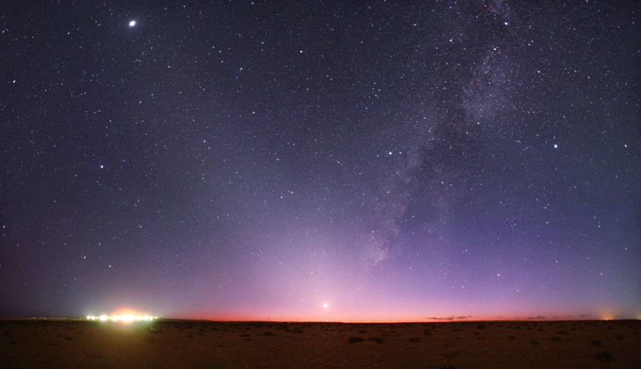 Am violettfarbigen Himmel sind viele Sternbilder zu sehen, sie sind beschriftet. Nach links steigt Zodiakallicht auf. Am Horizont links leuchten helle Stadtlichter. Rechts im Bild verläuft die Milchstraße diagonal nach oben.