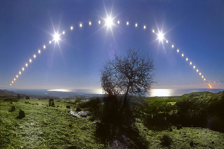 Hinter einer grünen Landschaft und dem Meer, das bis zum Horizont reicht, steigt in einem Bogen die Sonne auf, an drei Stellen ist sie heller mit Strahlenkranz abgebildet und geht am Bildrand im Abendrot unter. Mitten unter dem Sonnenbogen steht ein blattloser Baum.