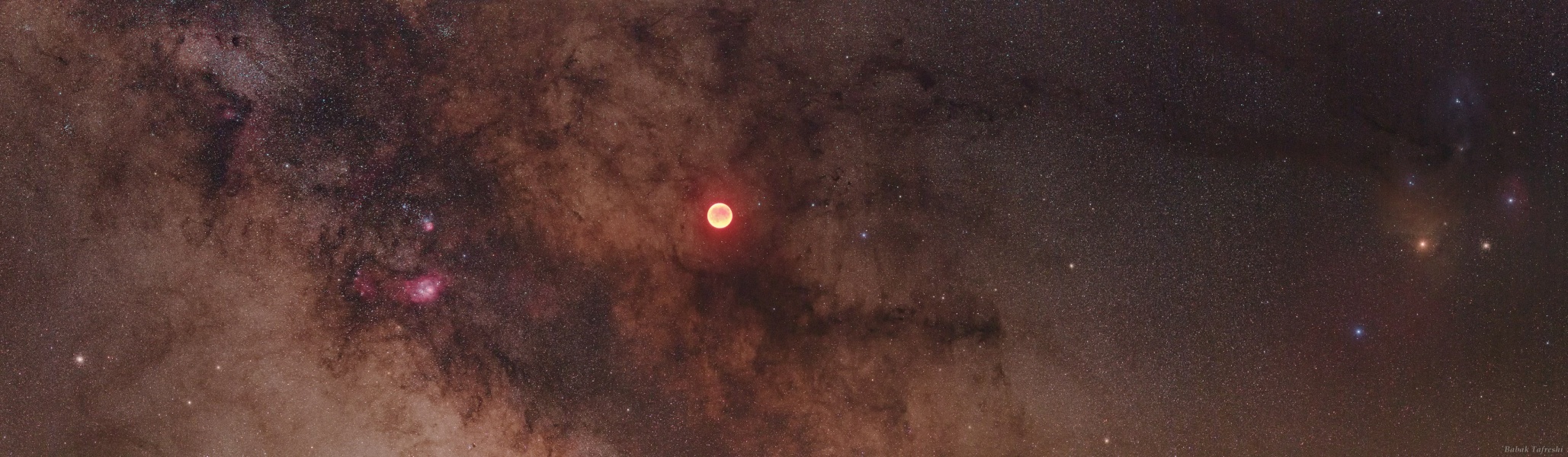 Am Himmel leuchtet zwischen Sternwolken und Dunkelnebeln der rote Mond bei einer totalen Mondfinsternis.