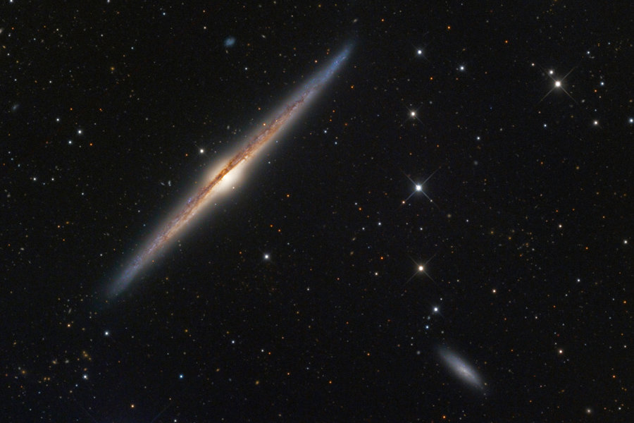 Wie eine Spindel wirkt die Galaxie in der linken oberen Ecke. Sie hat in der Mitte eine helle Wölbung undist von einem Staubwulst durchschnitten. Der Staubwulst läuft außen um die Galaxienscheibe und ist daher als Linie zu sehen. Rechts unten ist eine kliene, strukturlose Spiralgalaxie, die scheinbar an einer Sternenkette hängt.