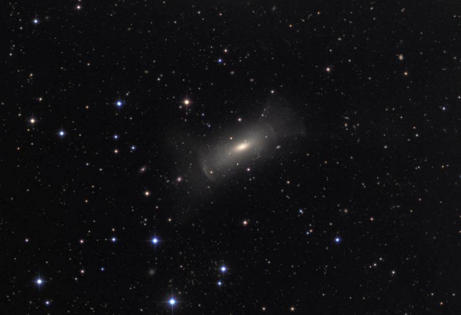 Mitten im Bild ist eine Galaxie zwischen dünn gesäten, bunten Sternen. Ihr leicht verschwommener Kern ist von einem diffusen Halo umgeben.