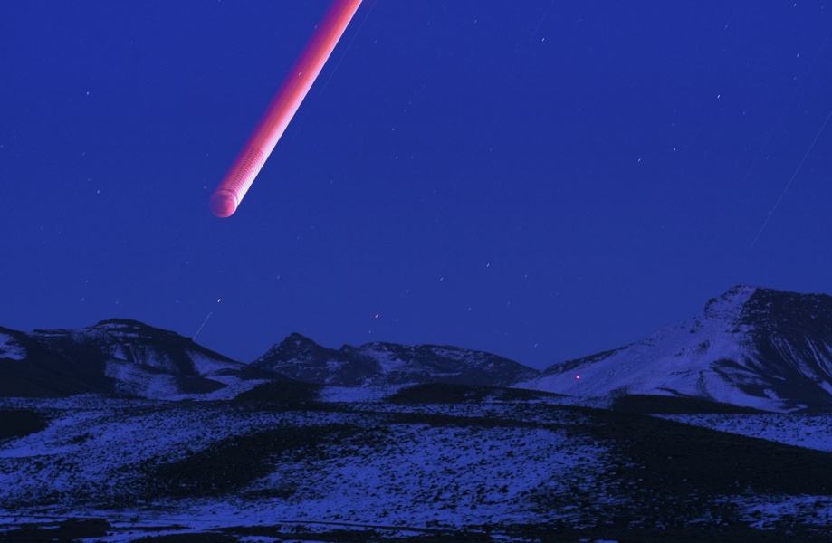 Über einer blauen Landschaft mit verschneiten Bergen steigt eine breite rote Spur auf, es ist der lang belichtete Mond, der links noch von der Sonne beleuchtet wird. Je höher er steigt, desto schmaler wird der von der Sonne beleuchtete Streifen.