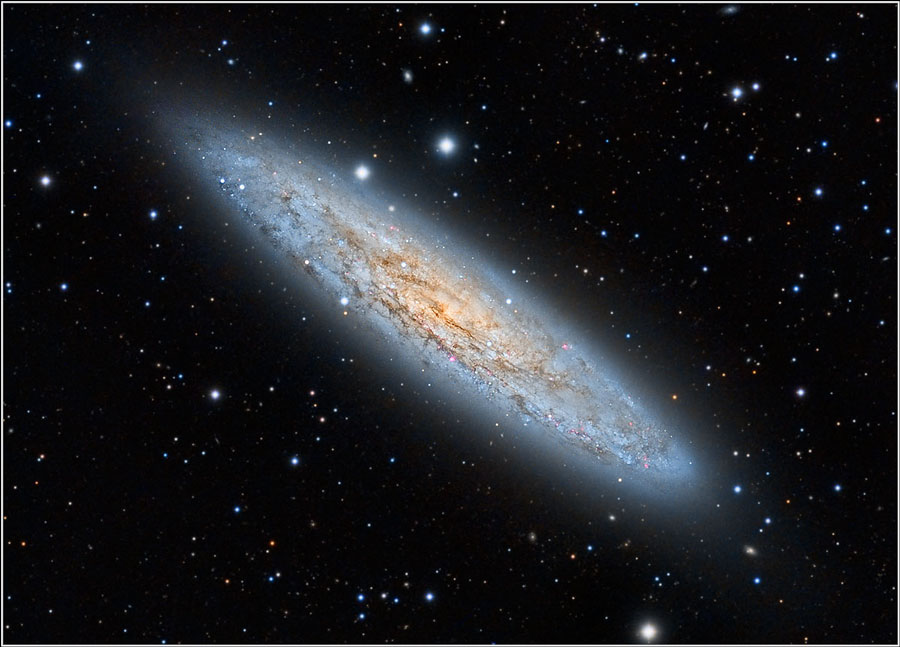 Eine scheibenförmige Spiralgalaxie, die von Staubbahnen gesprenkelt ist, liegt schräg im Bild.