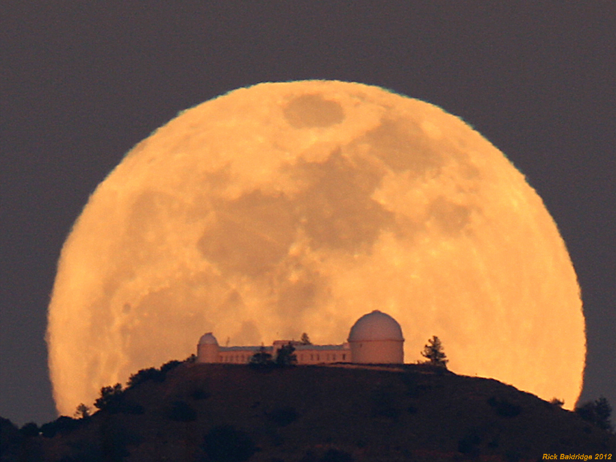 Vor der riesigen orangefarbenen Scheibe des Vollmondes ragt die Silhouette des Lick-Observatoriums auf.