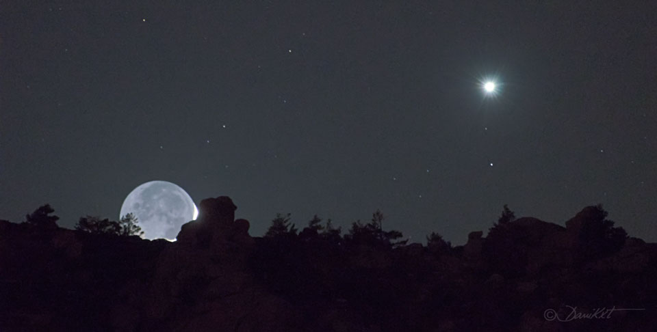 Hinter dem dunklen Horizont geht der Sichelmond unter, seine Nachtseite wird von der Erde beleuchtet. Rechts darüber strahlt der Planet Venus.