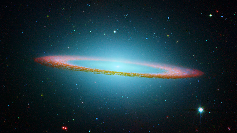 In der Bildmitte leuchtet ein cyanfarbener Nebel, der von einem flachen Staubring umgeben ist. Der Staubring wurde rosarot gefärbt.