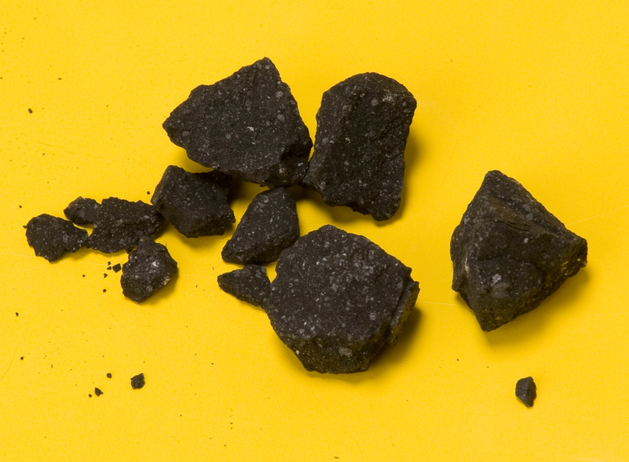 Auf einem gelben Grund liegen Bruchstücke eines Konglomerats aus Gestein, die kohlschwarz sind.