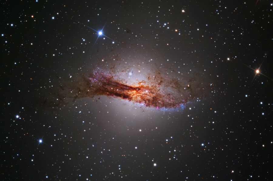 Die elliptische Galaxie Centaurus A ist von einem breiten, wüsten Staubband bedeckt. Im Bild ist sie von Sternen und einem diffus leuchtenden Halo umgeben.