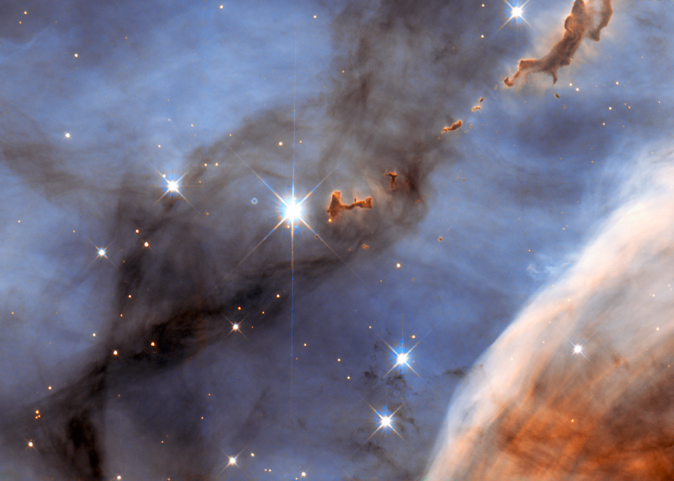 Dieser Ausschnitt des Carinanebels zeigt rechts oben sogenannte BLOBs, das sind dichte, undurchsichtige Molekülwolken. Der Hintergrund des Bildes leuchtet blau, rechts unten ist ein Stück von einem weißlich-rotbraunen Nebel zu sehen.