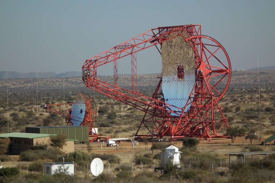 Mitten in einer kargen Buschlandschaft steht ein riesiges schwenkbares Teleskop. Der Spiegel wird von einem roten Gerüst gehalten und spiegelt die Landschaft verkehrt herum.