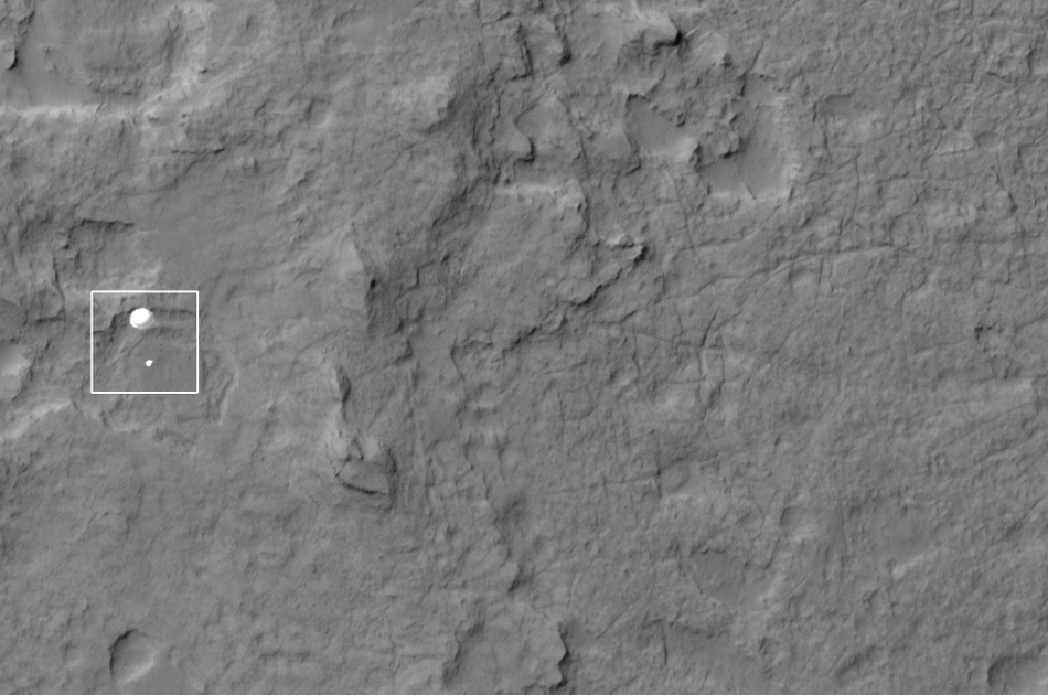 Der Marsrover Curiosity schwebt am Fallschirm zur Marsoberfläche hinab. Die Aufnahme stammt vom Mars Reconnaissance Orbiter. Im Hintergrund ist die Marsoberfläche zu sehen.
