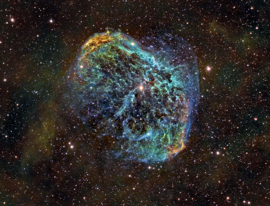 Von vielen eng verteilten großteils kleinen Sternen leuchtet ein stark gefaserter Nebel in blauen und türkisen Farbtönen. Es ist der Sichelnebel NGC 6888 im Sternbild Schwan.