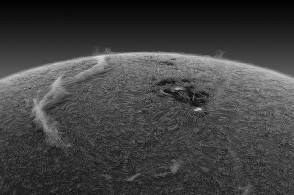 Die Sonne ist schwarzweiß und invertiert dargestellt, daher ist der Rand heller. Links schwebt eine riesige lange Protuberanz über der Oberfläche, rechts ist eine Sonnenfleckengruppe.