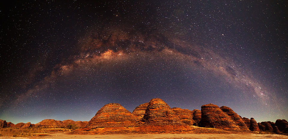 Über geschichteten roten Felskuppen, die an Bienenstöcke erinnern, wölbt sich das Zentralband der Milchstraße. Die Kuppen sind die Bungle Bungle in Westaustralien im Purnululu-Nationalpark.