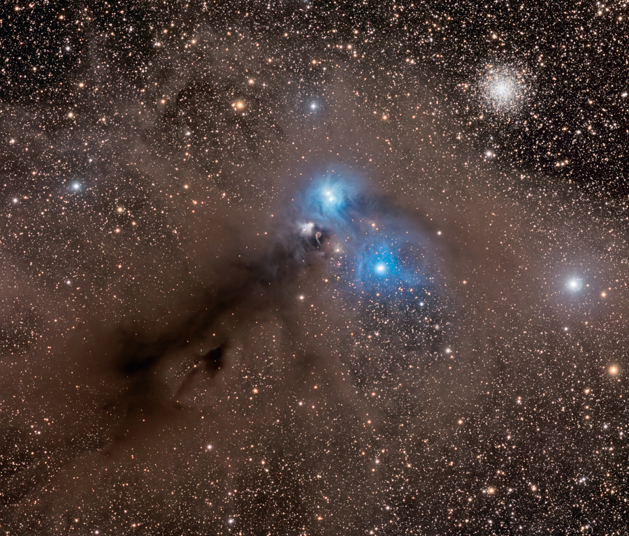 Von links unten breitet sich eine dunkle Staubwolke diagonal zur Mitte des Bildes aus, in der Mitte leuchten zwei helle Sterne von blauen Reflexionsnebeln umgeben. Recht oben leuchtet der Kugelsternhaufen NGC 6723.