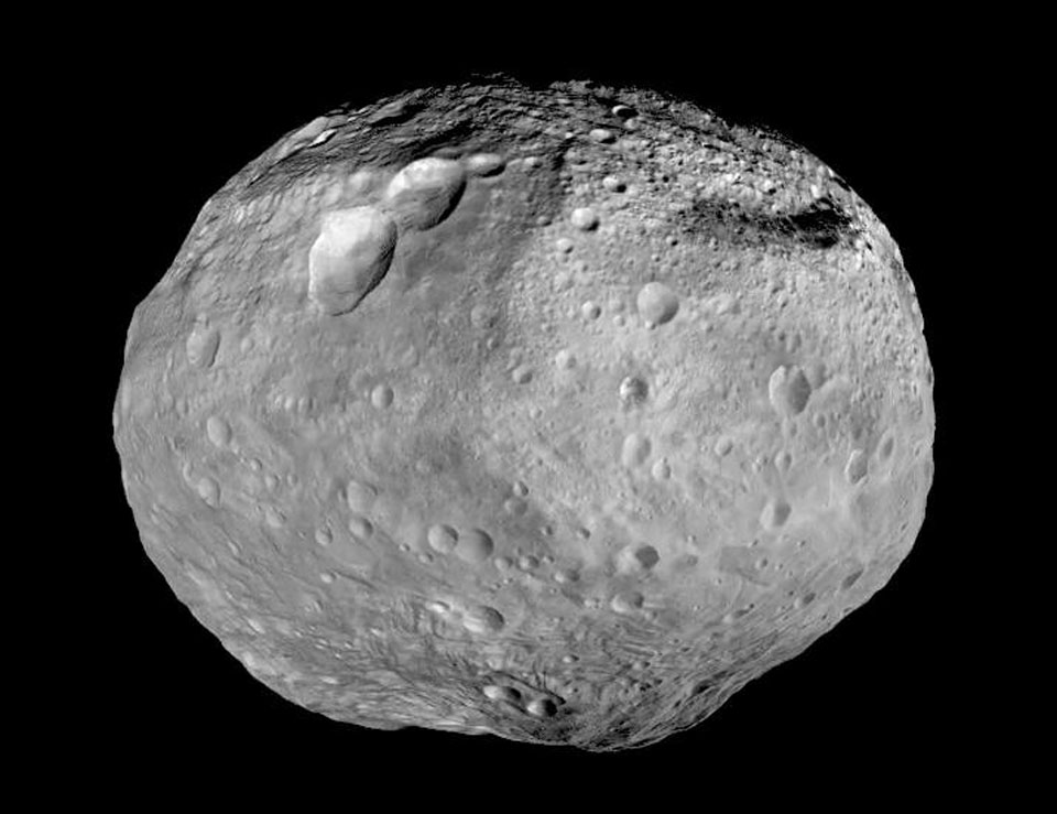 Wie eine zernarbte graue Kartoffel schwebt der Asteroid Vesta vor der Schwärze des Weltraums. Rechts oben sind viel mehr Krater als links unten. Am unteren Ende ist ein hoher Berg zu sehen, höher als der Mount Everest.