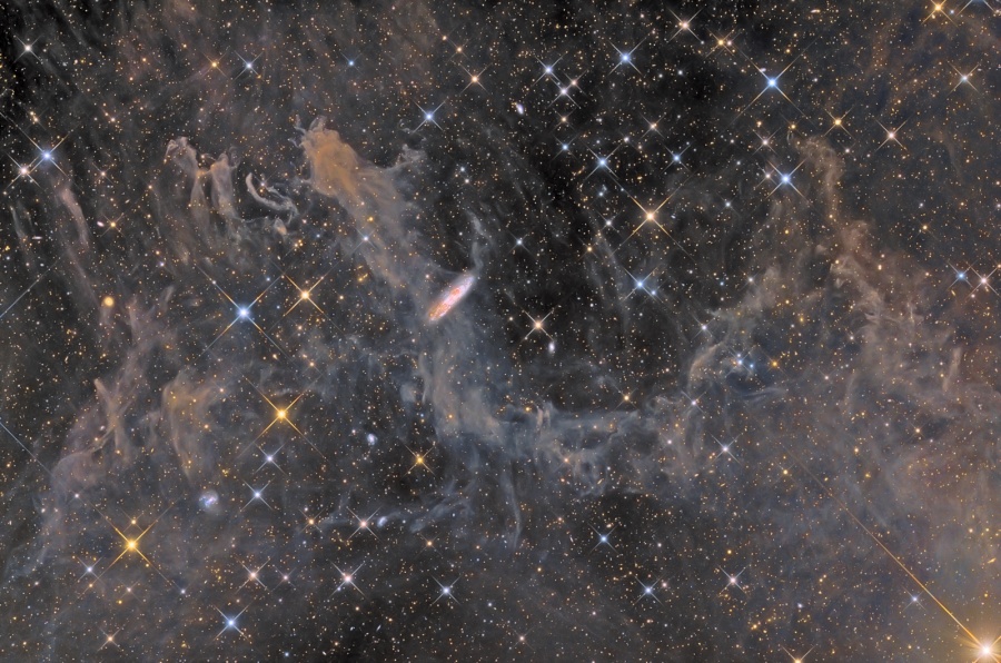 Helle, gezackte Sterne und einige weit entfernte Galaxien sind im Bild verteilt. Dazwischen liegen galaktische Federwolken, sie werden auch als integrierter Flussnebel bezeichnet. Die diffuse Wolke im Bild ist MBM 54.