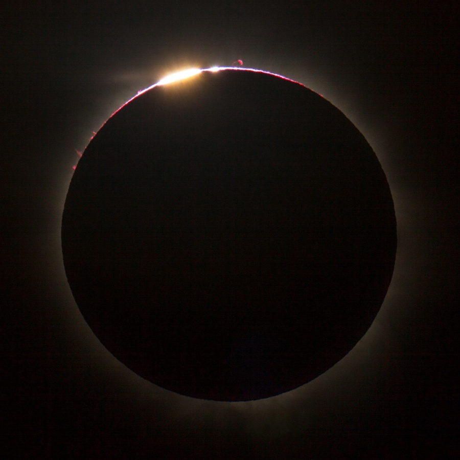 Der schwarze Kreis im Bild ist der Mond. Oben blitzt ein Scheibchen Sonne über den Rand, ein Diamantring und einige Bailysche Perlen. Oben ragen rote Protuberanzen über den Mondrand.