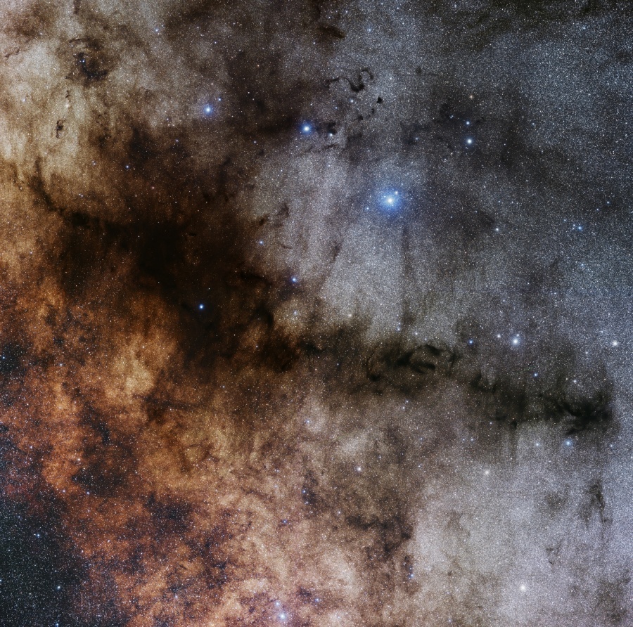 Die dunkle, ausgefranste Wolke im Bild vor einem Hintergrund aus dichten Sternen und Fasern von Dunkelnebeln erinnert entfernt an eine Pfeife.