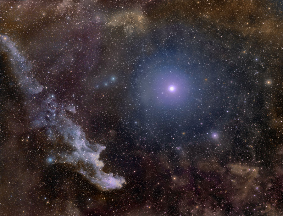 Der Hexenkopfnebel links im Bild blickt scheinbar zum hellen Stern Rigel im Orion mitten im Bild, der von einem blauen Hof umgeben ist.