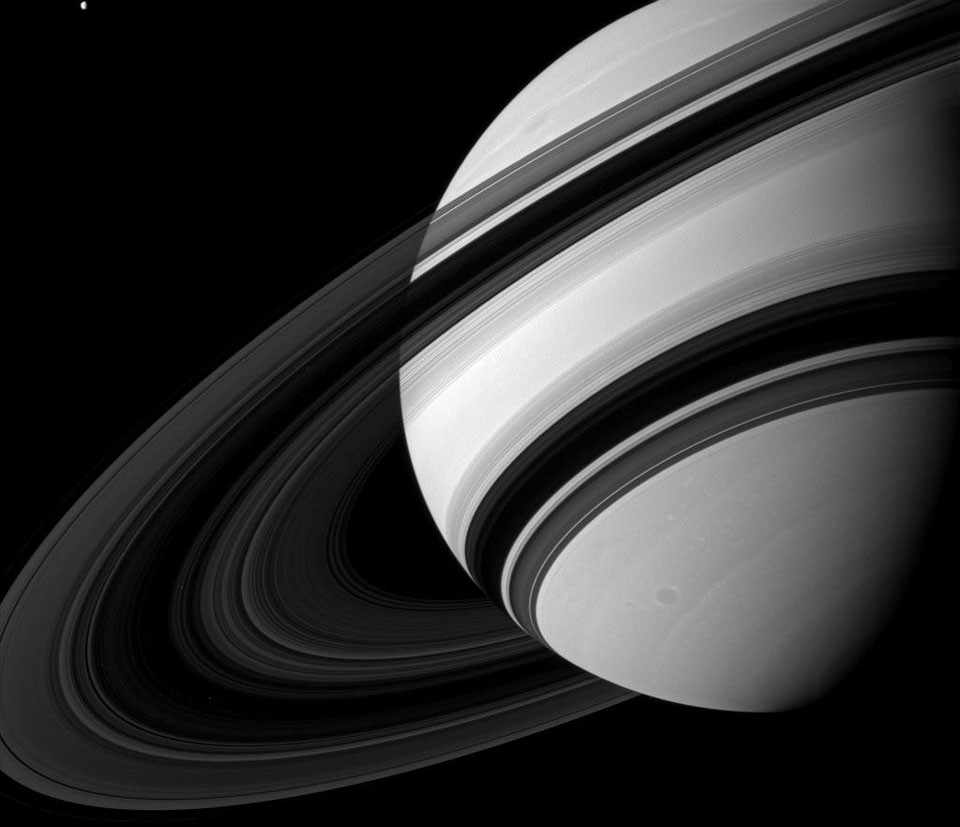 Rechts oben ist der Planet Saturn (angeschnitten), die Ringe befinden sich links oben und werfen Schatten nach unten auf den Planetenkörper. Die Ringe sind von hinten beleuchtet, weil die Sonne höher steht.