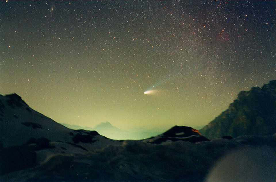 Über dem Valparolapass in den italienischen Dolomiten leuchtet der Komet Hale-Bopp vor einem sternklaren Himmel, der von unten durch Licht beeinträchtigt ist. Seine beiden mächtigen Schweife sind gut erkennbar.