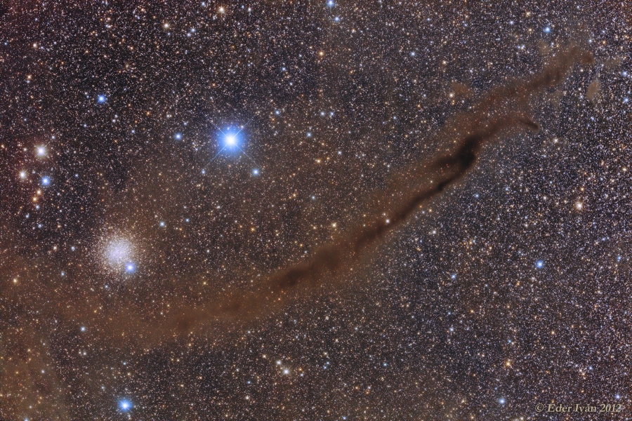 Vor einem dicht gedrängten Sternenfeld verläuft ein dunkelbrauner Nebel, das "Dunkle Dingsda". Links darüber leuchtet der Kugelsternhaufen NGC 4372 und ein bläulicher Stern.