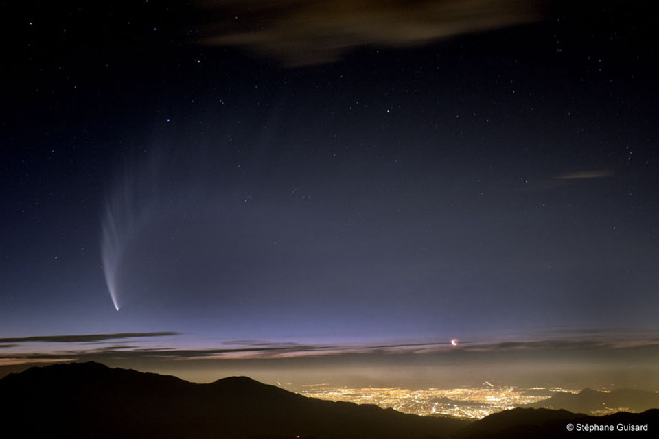 Über der hell erleuchteten Stadt Santiago de Chile steht knapp über dem Horizont der Sichelmond. Von links breitet Komet McNaught seinen gefächerten Staubschweif aus.