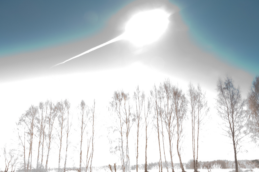 Über den Silhouetten blattloser Bäume strahlt ein gleißend heller Blitz, der Himmel hinter den Bäumen ist weiß.