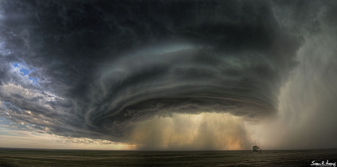 Ein dunkler Wolkenturm füllt das Bild. Unten stürzt Regen und Staub aus einer riesigen trichterförmigen Wolke.
