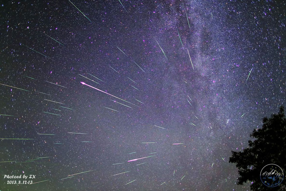 Am sternklaren Himmel steigt rechts die Milchstraße auf. Im Vordergrund strömen viele Meteore von einem Punkt im Sternbild Perseus aus.