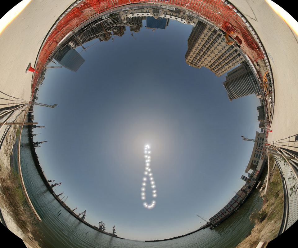 Das Kugelpanorama zeigt den Hafen von Baku in Aserbaidschan. Am blauen wolkenlosen Himmel zeichnet die Sonne die 8-förmige Schleife eines Analemmas.