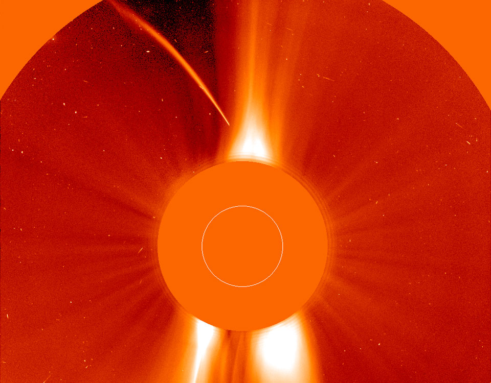 Mitten im Bild verdeckt eine orangefarbene Scheibe die Sonne. Helles Licht strömt dahinter hervor. Links oben ist der gekrümmte Schweif eines Kometen zu sehen, der sich der Sonne nähert.