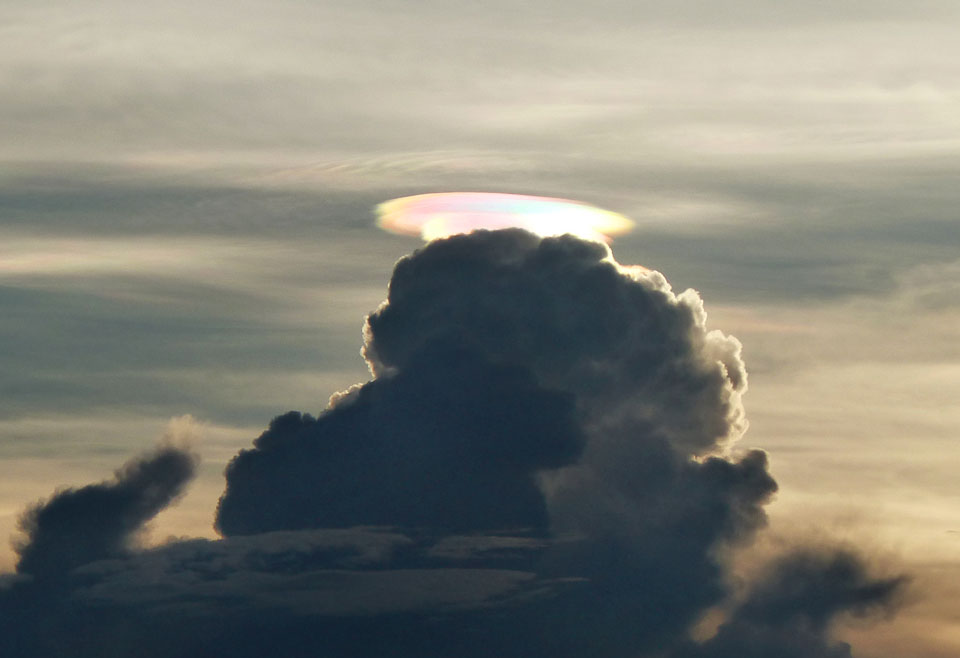 Ein dunkler Wolkenberg hat eine helle, schillernde Wolkenkappe. Darüber sind gewellte Wolken zu sehen.