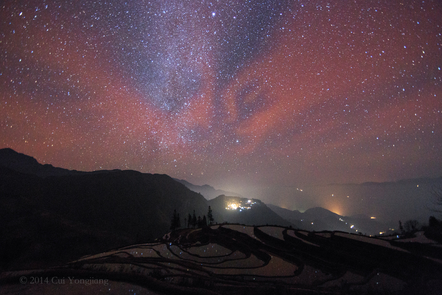 Über bewässerten Reisterrassen in der chinesischen Privinz Yuanyang leuchtet ein intensives Nachthimmellicht am sternklaren Himmel.