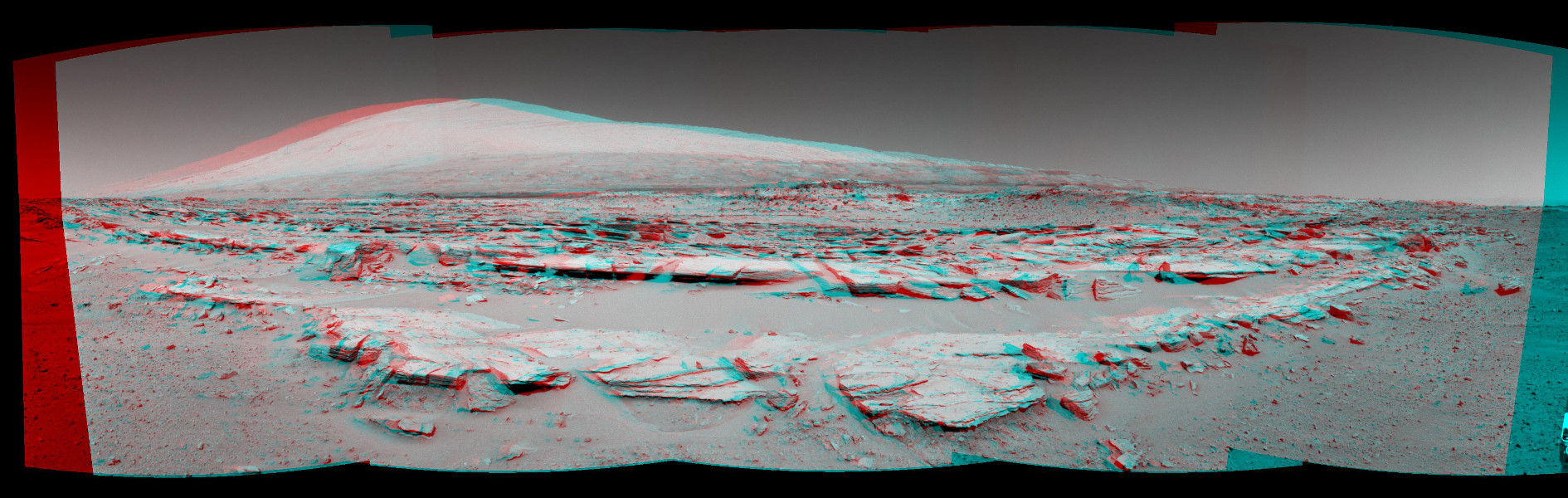 Das Bild ist rot-cyanfarben. Wenn man es mit Brillen in diesen Farben betrachtet, wirkt es dreidimensional. Es zeigt geologische Schichten im Vordergrund. Hinten ragt Mount Sharp (Aeolis Mons) auf.