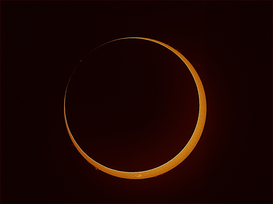 Die orangefarbene Sonne ist fast ganz vom Mond verdeckt. Ein schmaler sichelförmiger Teil der Sonne ist sichtbar. Der Mond berührt rechts oben den Sonnenrand.