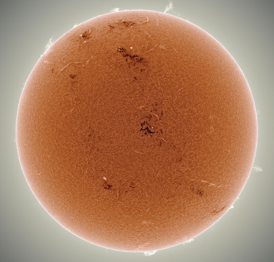 Das Bild der Sonne wurde invertiert und eingefärbt. Daher ist der orangefarbene Ball in der Mitte dunkler und am Rand sehr hell. Am Rand ragen helle Sonnenfackeln auf, in der Mitte und oben sind größere dunkle Regionen.