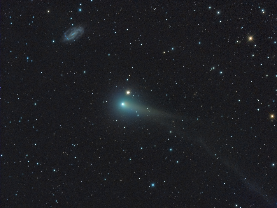 Das Bild enthält lose verteilte Sterne. In der mitte leuchtet ein kleiner Komet mit grünlicher Koma und Schweif neben einem etwa gleich hellen Stern, links oben befindet sich eine kleine, schwach leuchtende Spiralgalaxie.