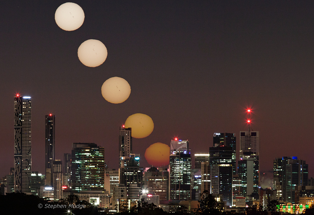Hinter der Silhouette der australischen Stadt Brisbane geht die Sonne auf. Die Sonnenscheiben des Kompositbildes steigen links immer höher.