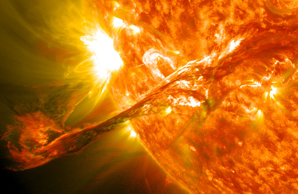 Die Sonne ragt von rechts oben ins Bild. Am Sonnenrand links neben der Mitte bricht ein sehr helles Filament aus. Aus diesem dringen Plasmaschleifen, die vom Magnetfeld gelenkt werden. Darunter ist eine riesige Sonnenfackel, die weit über den Sonnenrand hinausreicht.