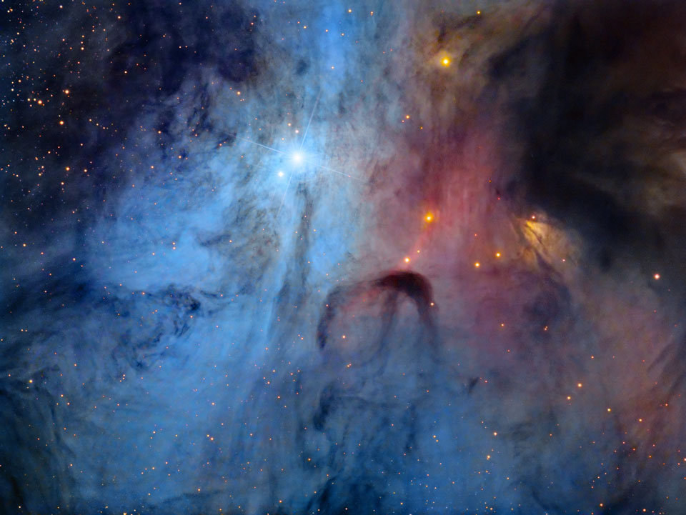 Blauer Staub und dunkle Fasern bedecken das Bild wie ein impressionistisches Gemälde. Rechts leuchten Sterne aus dem Inneren der Staubwolke und färben die Wolke rot.