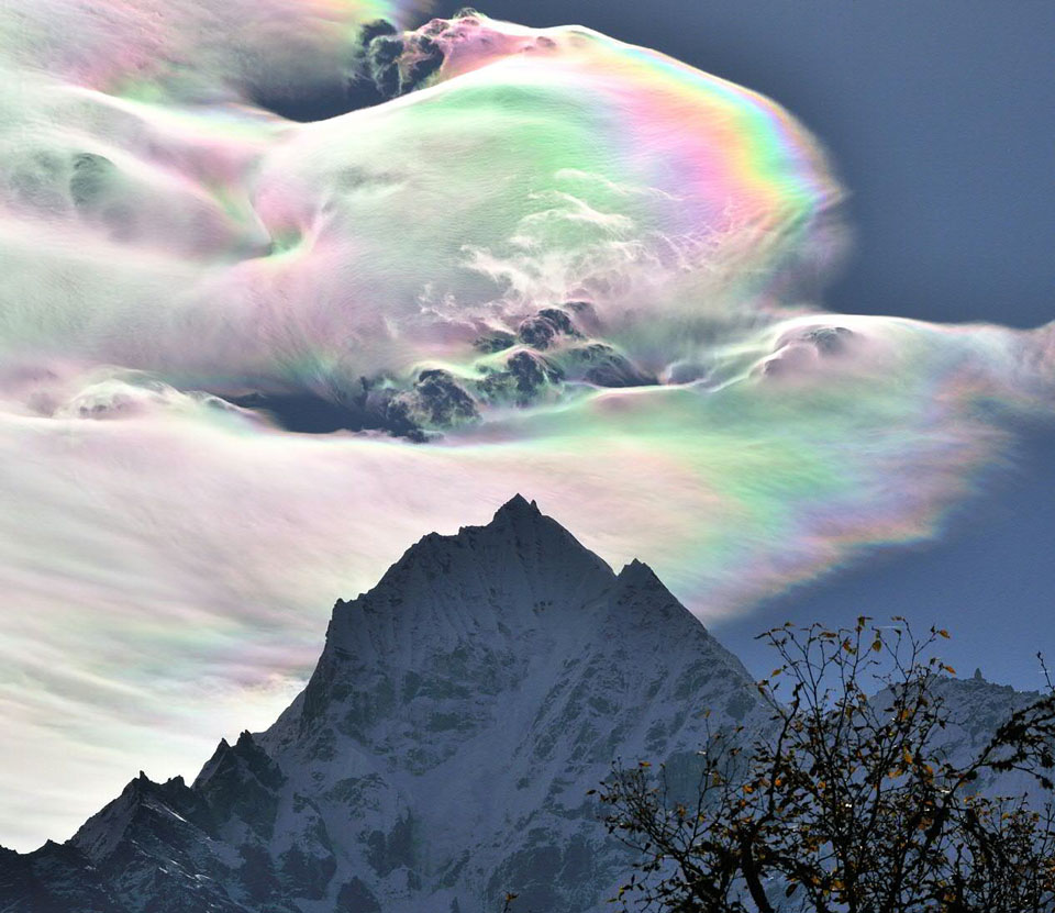 Über einem Gipfel im Himalaya schillern irisierende Wolken in vielen Farben des Spektrums.