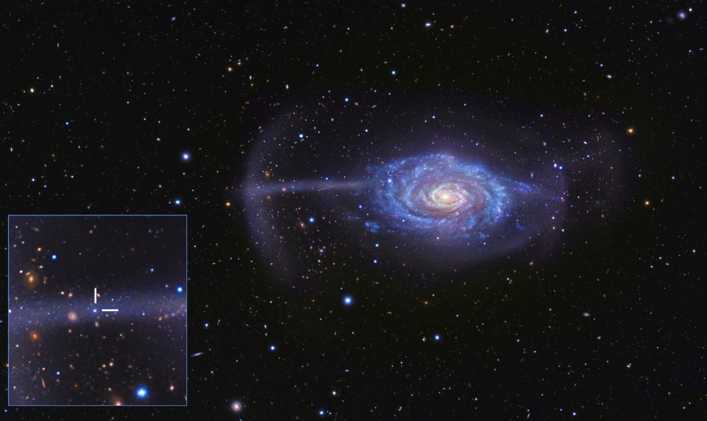 Die Spiralgalaxie in der Mitte wirkt relativ normal, doch links ragt ein blasser blauer Sternstrom aus der Scheibe, der an einen Schirm erinnert. Links ist ein Bildeinschub, er zeigt den Kern der kleinen Galaxie, aus der der Gezeitenstrom entstand.