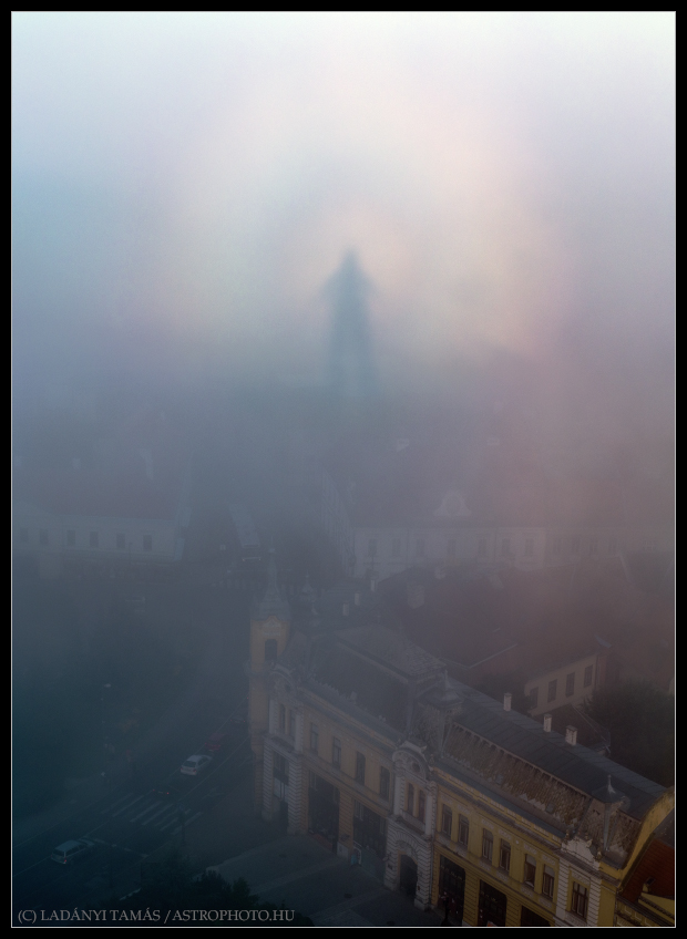Über den Dächern der ungarischen Stadt Veszprém schwebt eine geisterhafte Silhouette, die von hellen Bögen umgeben ist, auf einer Nebelschwade.