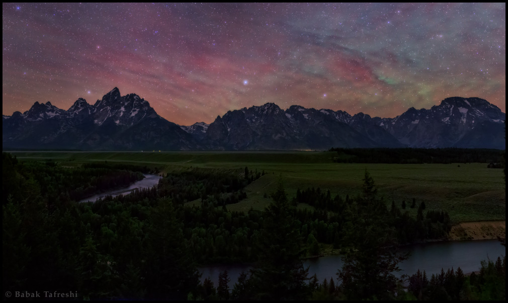 Über einer Gebirgskette ist der Himmel von Sternen und rot schimmernden Wolken überzogen. Im Vordergrund ist ein Fluss, der Snake River.