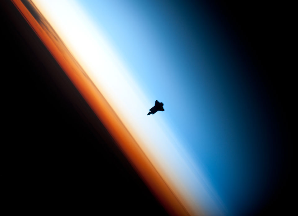 Das bekannte Bild zeigt die Erde links unten, darüber verläuft diegonal im Bild ein orangefarbener Streifen, darüber ein breiterer weißer Streifen, danach folgt blau, das in Schwarz übergeht. Am Übergang vom weißen zum blauen Streifen ist die Silhouette einer Raumfähre.