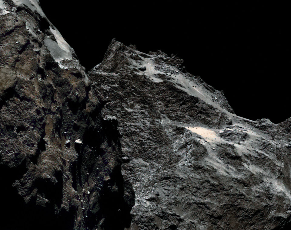 Die Oberfläche des Kometen 67P/Tschurjumow-Gerassimenko ist zerklüftet und dunkel wie Kohle. Das Farbbild wirkt schwarz-weiß.