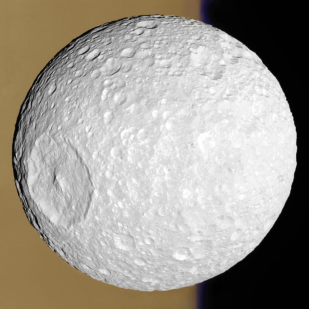 Vor dem ockerfarbenen Saturn, der den halben Hintergrund füllt, ist der Saturnmond Mimas zur Gänze abgebildet. Links ist sein berühmter Krater Herschel mit Zentralberg zu sehen.